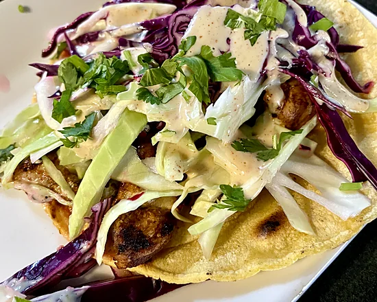 Corn tortilla tacos topped with red and green cabbage slaw, cilantro and creamy sauce
