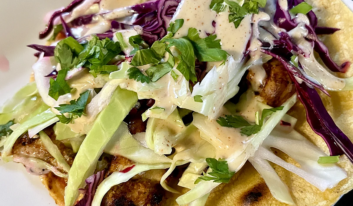 Corn tortilla tacos topped with red and green cabbage slaw, cilantro and creamy sauce